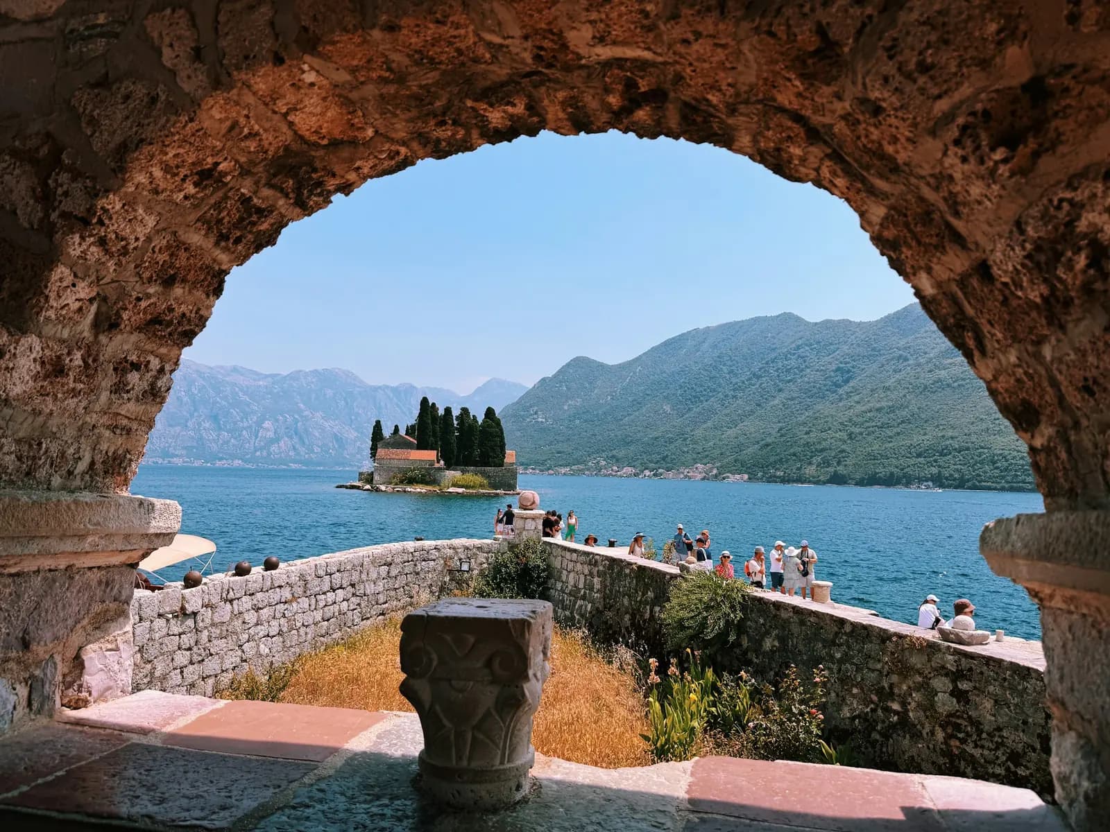 A stone arch framing the water and mountains near Perast.