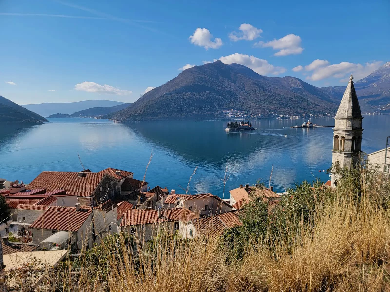 Tiled rooftops and a bell tower in Perast overlooking the Bay of Kotor and mountains.